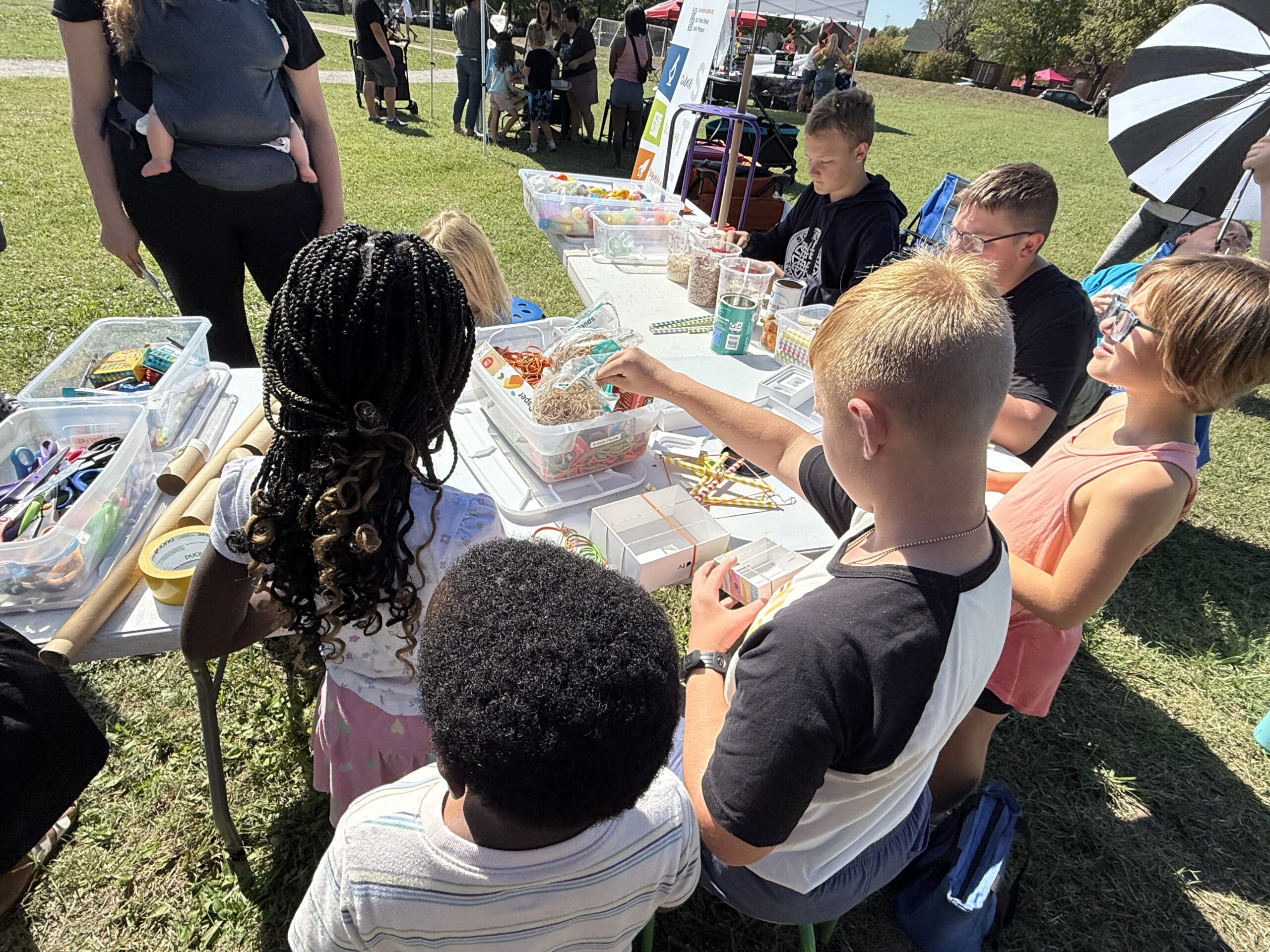 several elementary school age kids gathered around a table outside doing a hands-on activity