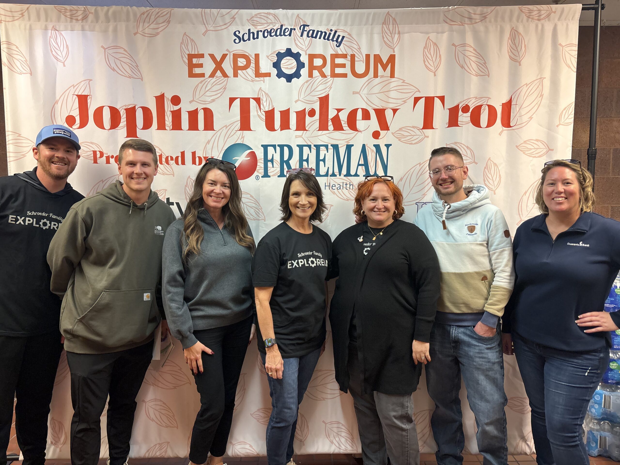 Seven adult organizers lined up in front of a banner that says "Exploreum Joplin Turkey Trot"